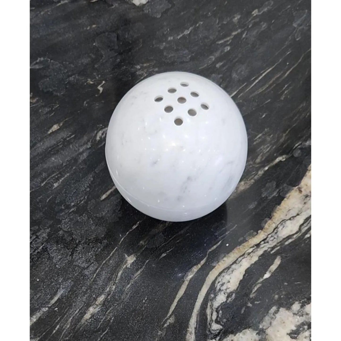 Carrara white marble sphere incense burner with natural veining on a black desk