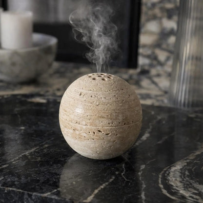 Beige travertine marble sphere incense burner in natural stone with round minimalist design for luxury home decor and aromatherapy with smoke coming out